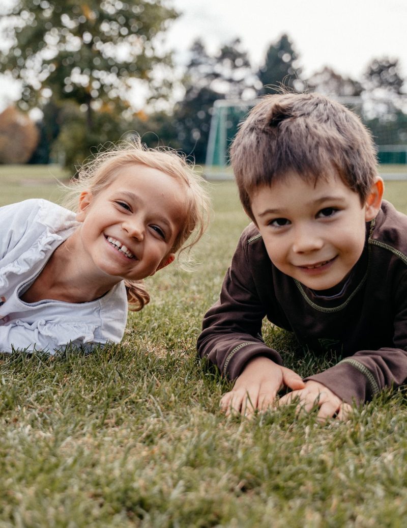 Zwei Grundschulkinder liegen lächelnd auf der Wiese vor dem Fußballtor, St.-Michael-Grundschule Neu-Ulm