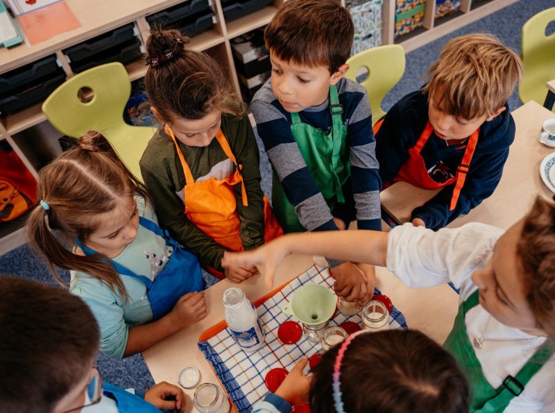Grundschulkinder mit Schürzen füllen gemeinsam Joghurt in Gläser, St.-Michael-Grundschule Neu-Ulm